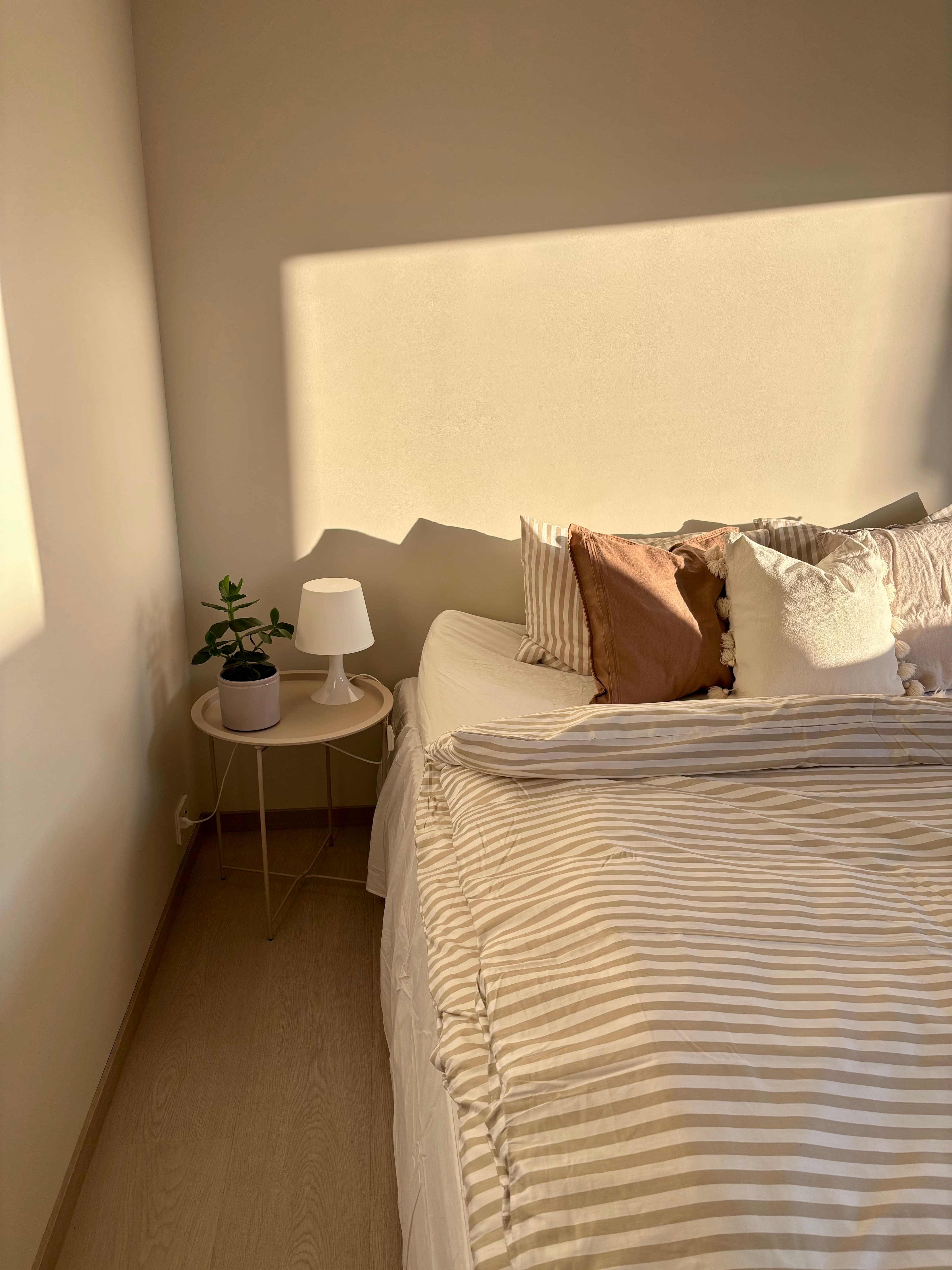 Sengedetaljer med nattbordlampe og plante i mykt morgenlys